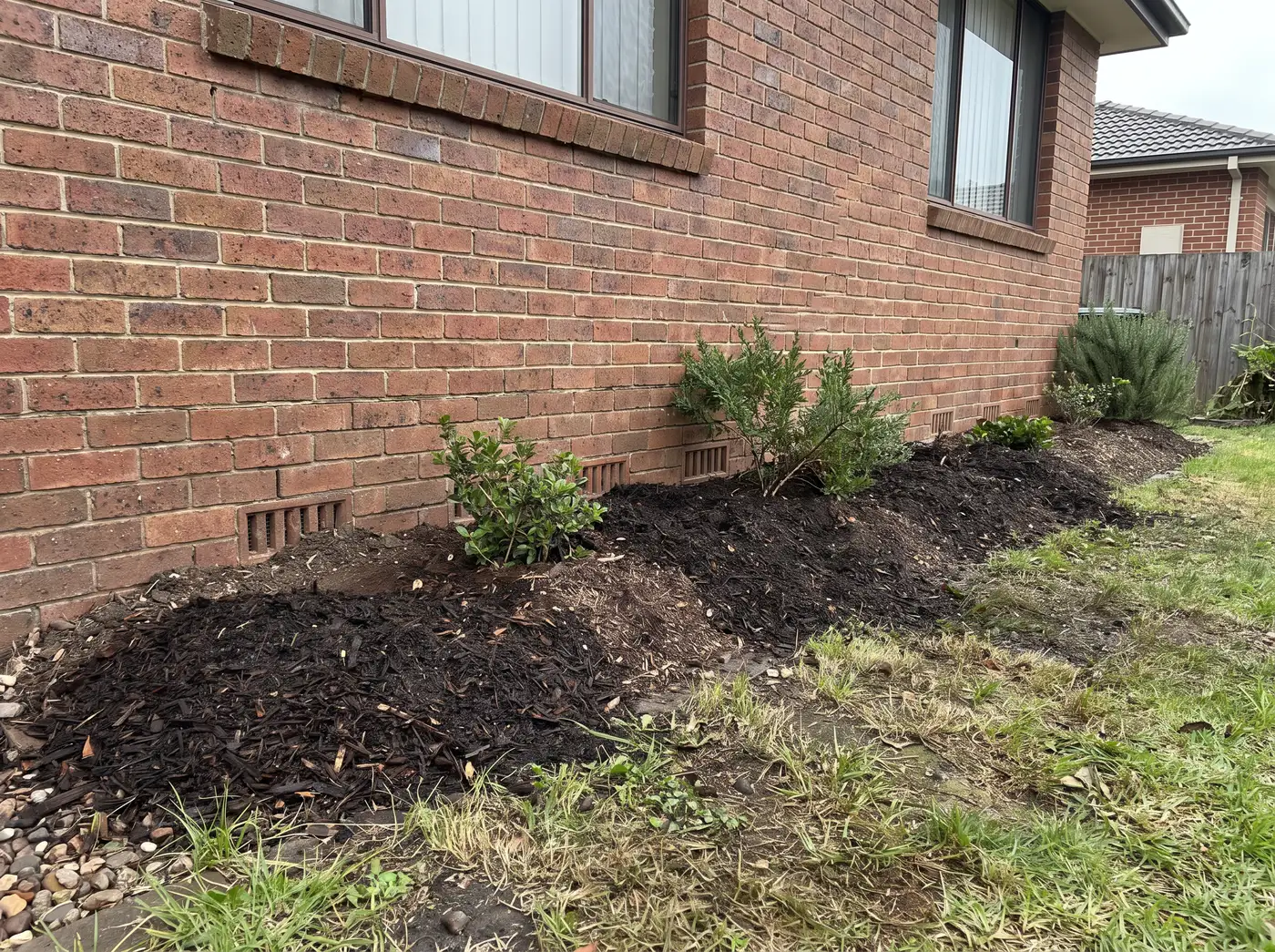 Garden mulch mounded up against a brick house wall, part-burying the subfloor vents