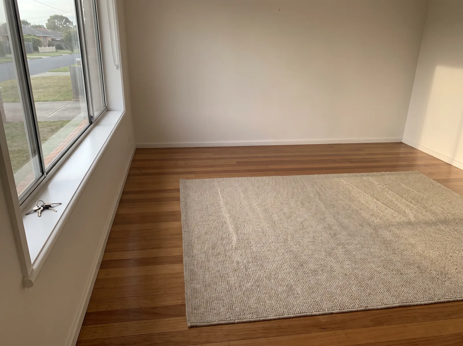An empty, freshly cleaned rental living room at handover, keys on the windowsill and fresh vacuum lines in the rug
